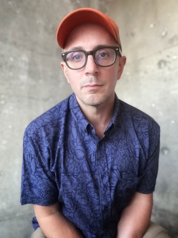 Photo of Steven Burns, a white male wearing black glasses, a red hat, and a blue shirt